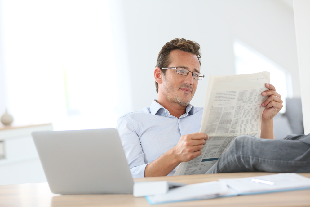 Man reading newspaper with stretched legs over table-1